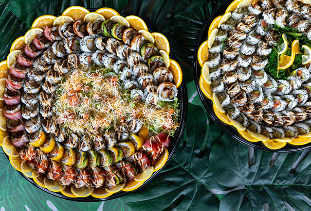 Two large platters of sushi rolls arranged for catering