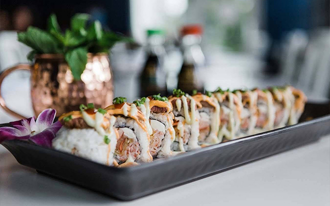 A long platter of sushi rolls drizzled with sauce
