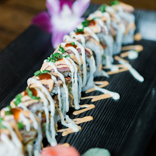 A row of sushi rolls drizzled with sauce