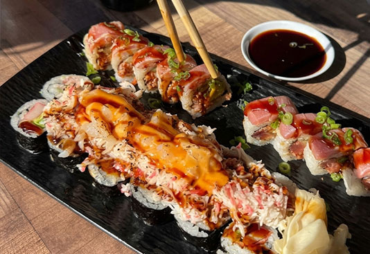 Chopsticks lifting a sushi roll beside a bowl of dipping sauce