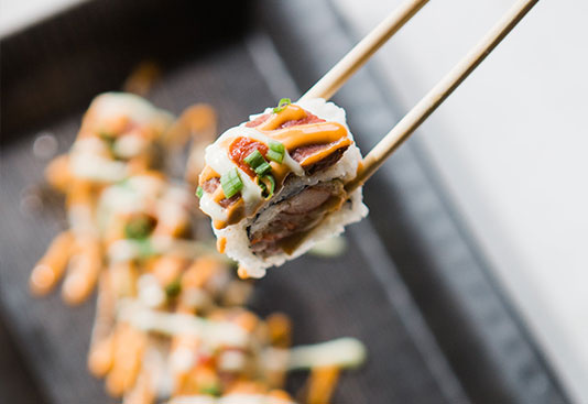 Chopsticks holding a sushi roll above a serving platter