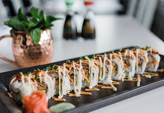 A long sushi platter with sauce drizzled across the rolls